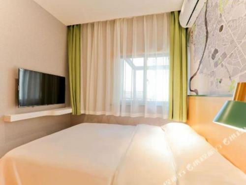 a bedroom with a bed and a tv and a window at Vatica Hotel Hefei Yaohai Longgang Subway Station in Hefei