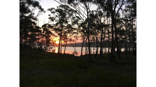 a sunset over a body of water with trees at Banyula Cove by Tiny Away in Barnes Bay