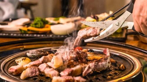 a person is cooking meat on a grill with a knife at Jeju EQ Stay in Jeju