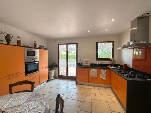La cuisine est équipée d'armoires orange et d'un four avec plaques de cuisson. dans l'établissement Villa pour 8 avec clim et parking proche de la mer, à Lunel