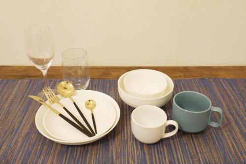 a table with plates and cups and wine glasses at blue sea and house in Nanjo