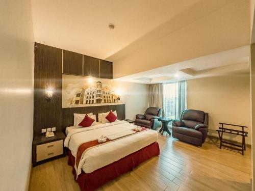 a hotel room with a large bed and two chairs at Hermes Palace Hotel Medan in Medan