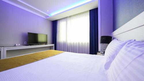 a bedroom with a white bed and a tv at Galaxy Hotel in Jeju