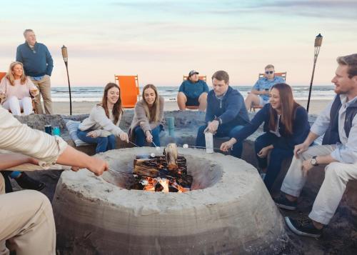 a group of people sitting around a fire pit on the beach at Seashells to Sandcastles 156 BAR in Mustang Beach