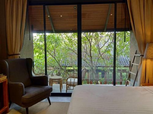 a bedroom with a bed and a chair and a window at Phingphayla Photharam in Ratchaburi