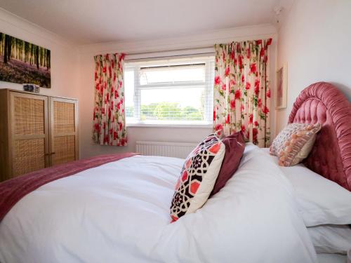 Un dormitorio con una cama blanca con cabecero rosa y una ventana. en Lavender Cottage, en Hailsham