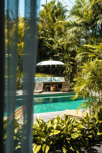 a swimming pool with two chairs and an umbrella at Amar Boutique Hotel in Canggu