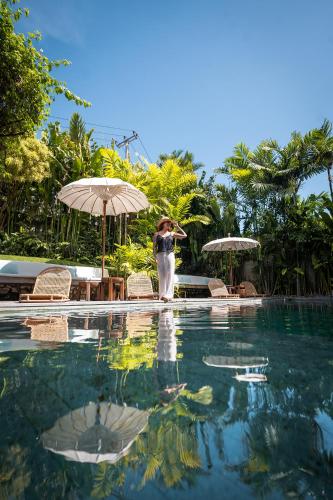 a woman is standing next to a swimming pool at Amar Boutique Hotel in Canggu