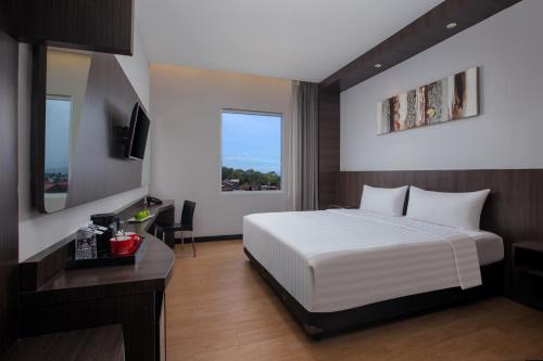 a bedroom with a bed and a desk and a television at Neo Dipatiukur Bandung by ASTON in Bandung