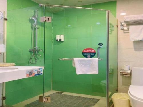 a green bathroom with a glass shower with a toilet at GreenTree Inn Langfang GuAn County Xinyuan Street Express Hotel in Langfang
