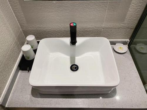 a white sink in a bathroom with two cups at GreenTree Inn Ganzhou Gan County Bus Station in Ganzhou