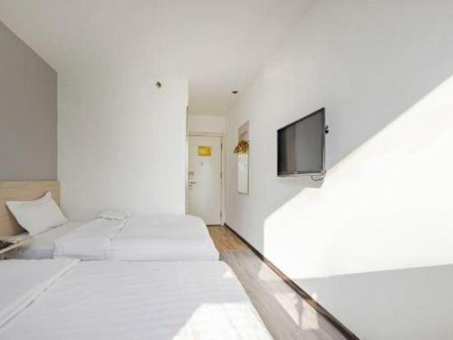 a white room with two beds and a flat screen tv at 7 Days Inn Tianjin Binhai New District Yujiabao Metro Station in Binhai