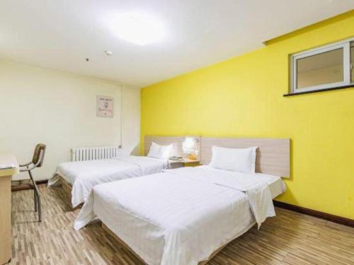 two beds in a room with a yellow wall at 7 Days Inn Tianjin Binhai New District Yujiabao Metro Station in Binhai