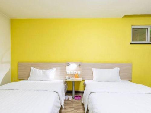two beds in a room with a yellow wall at 7 Days Inn Tianjin Binhai New District Yujiabao Metro Station in Binhai