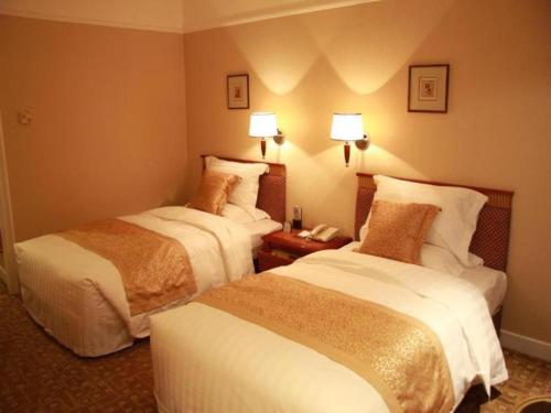 two beds in a hotel room with lamps on the wall at Jianguo Garden Hotel in Beijing