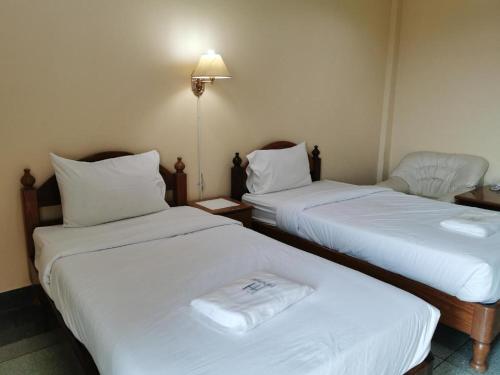 two beds in a room with white sheets and a chair at Hihotel Saraburi in Sara Buri