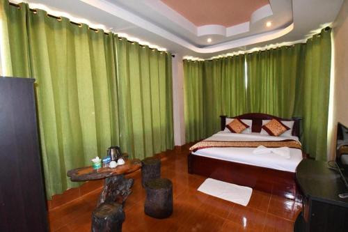 a bedroom with green curtains and a bed and a table at PXT Hotel in Ban Sivilai