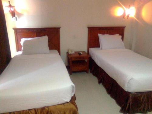 a bedroom with two beds and a night stand with two lamps at Yusro Hotel Restaurant & Convention in Jombang