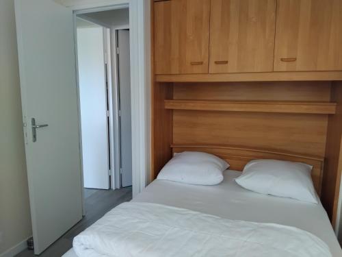 a bed with a wooden headboard and two pillows at Appartement refait à neuf en 2025 in Cabourg