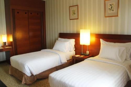 two beds in a hotel room with two lamps at Labersa Grand Hotel &Convention Center in Pekanbaru