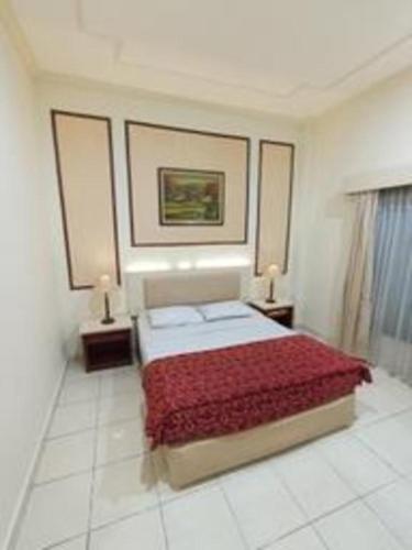 a bedroom with a bed with a red blanket and two lamps at Larisae Setia Kawan Hotel in Solo