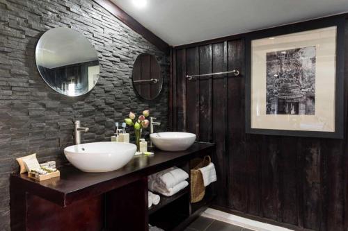 a bathroom with two sinks and a stone wall at Sampeah Retreat Villa in Phumĭ Trâpeăng Treăng