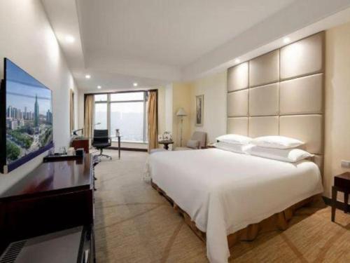a bedroom with a large white bed and a television at New Century Grand Hotel Zhuji Yaojiang in Shaoxing