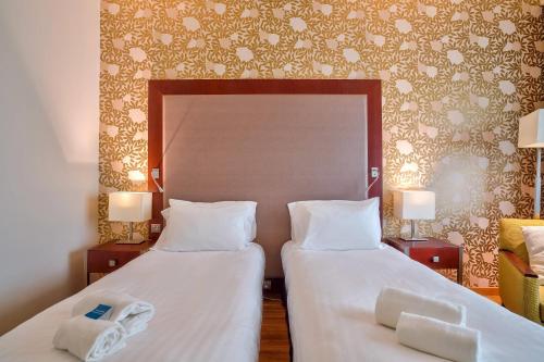 two beds in a hotel room with white sheets at Clarion Paris CDG Airport in Roissy-en-France