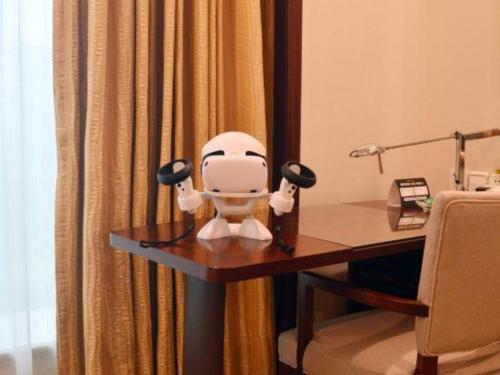 a white robot sitting on a desk in a room at New Century Grand Hotel Zhuji Yaojiang in Shaoxing