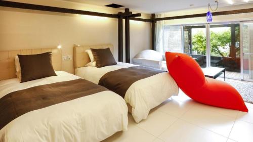 a bedroom with two beds and a red chair at Kyoto Keburikawa Hotel in Kameoka