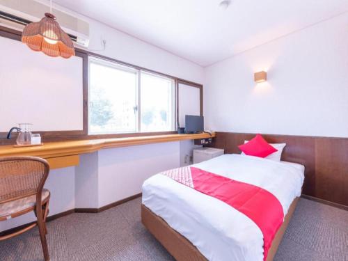 a bedroom with a bed and a desk and windows at Tabist Hotel Sankoen in Hitachi