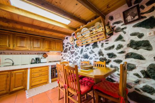 cocina con mesa, sillas y pared de piedra en Adega Velha en Calheta de Nesquim
