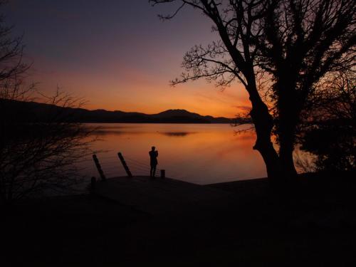 a person standing next to a lake at sunset at The Inn on Loch Lomond in Luss
