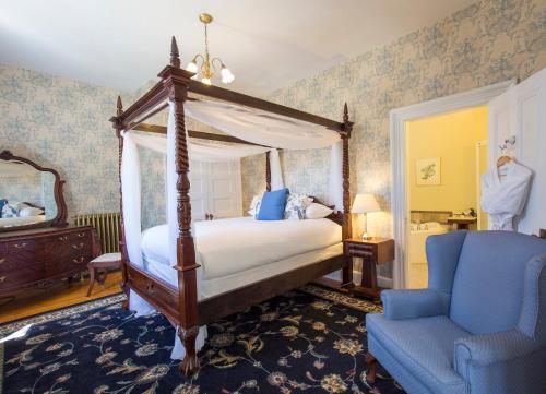 a bedroom with a canopy bed and a blue chair at Queen Anne Inn in Annapolis Royal