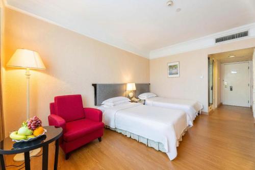a hotel room with two beds and a red chair at Shantou Golden Gulf Hotel in Shantou
