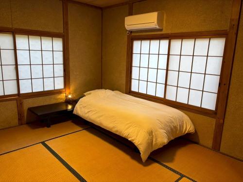 une chambre avec un lit dans une pièce avec deux fenêtres dans l'établissement 古民家宿りらいふ, à Kitsuki