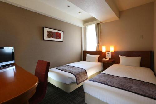a hotel room with two beds and a desk at Hotel Hokke Club Kumamoto in Kumamoto