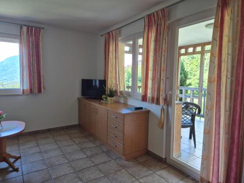 a room with a dresser with a television and a balcony at Apartmenthaus am Waalweg in Caines