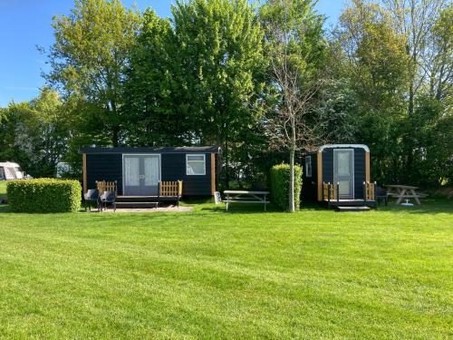 a cabin in the grass with two benches and a picnic table at Pipowagens Schotererf in Kuinre