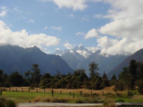 a field with mountains in the background with a fence at Ivorytowers Accommodation in Fox Glacier