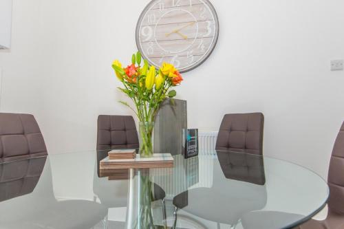 una mesa de cristal con un jarrón de flores y un reloj en Raleigh by Pureserviced, en Plymouth