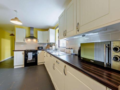 a large kitchen with white cabinets and black appliances at 5 bed in Brynteg 75907 in Llanwenog