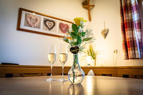two wine glasses and a vase with a flower in it at Thalerbauer Ferienwohnungen in Wackersberg