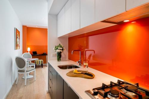 cocina con pared de color naranja y fogones en Oaks Melbourne South Yarra Suites, en Melbourne