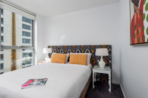 a bedroom with a white bed with orange pillows and a window at Oaks Melbourne South Yarra Suites in Melbourne