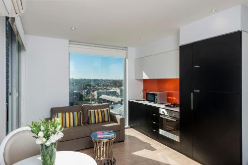 a kitchen and living room with a couch and a table at Oaks Melbourne South Yarra Suites in Melbourne