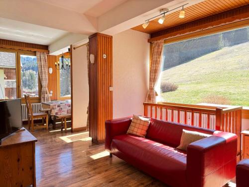 - un salon avec un canapé rouge et une grande fenêtre dans l'établissement Appartement cosy 8 pers avec terrasse, proche des pistes, Les Gets - FR-1-623-368, aux Gets