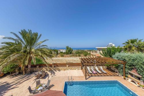 a swimming pool with chairs and palm trees and the ocean at Villa Agathi in Argaka
