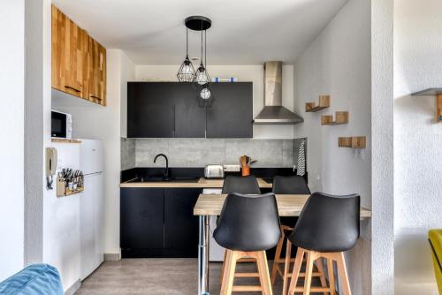 une cuisine avec des placards noirs et une table avec des tabourets dans l'établissement Le refuge du Gambetta - Proche Cité Médiévale & Bastide - NOUVEAU !, à Carcassonne