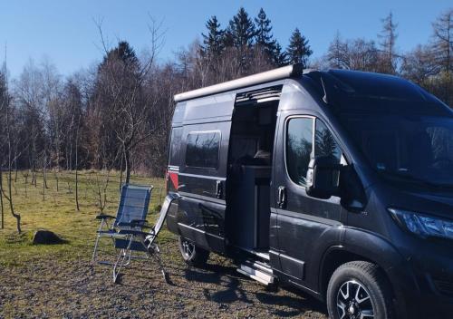 a black van parked in a field with a chair at destinature Dorf Südeifel in Ernzen